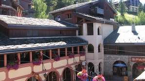 A traditional chalet-style building with a balcony and flower baskets, surrounded by forested mountains.