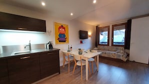 A compact kitchen with a modern sink, a dining area with a table and chairs, a wall-mounted TV, and a window with curtains.