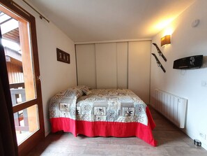 A bedroom with a bed, a window, a radiator, and a wall-mounted TV.