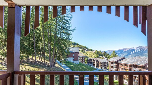 A wooden balcony with a view of a mountain resort, including buildings and trees. - Charming 2-room apartment for 5 in La Plagne with balcony and equipped kitchen (La Plagne)