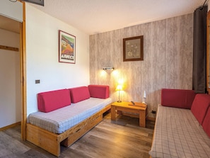 A cozy room with a wooden bed, a red sofa, and a small table with a lamp. - Divisible studio for 4, direct slope access (La Plagne)