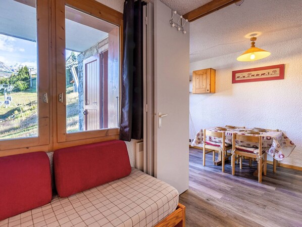 A cozy room with a wooden bench, a dining table with chairs, and a view of a mountainous landscape through a window. - Divisible studio for 4, direct slope access (La Plagne)
