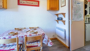 Un comedor con una mesa dispuesta para cuatro personas, sillas de madera, una lámpara de techo, un cuadro enmarcado y un mapa en la pared.