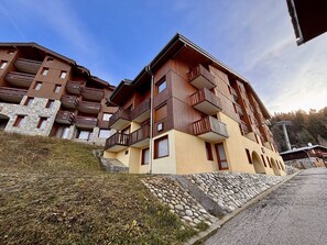 Hotel com vários andares, varandas, fachada de pedra e entrada pavimentada.