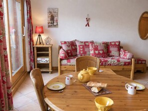A cozy living room with a wooden sofa, a dining table with yellow cups and a bread roll, and a red lamp on a side table. - Charming 2-bedroom apartment in Méribel, close to slopes and shops (Méribel)