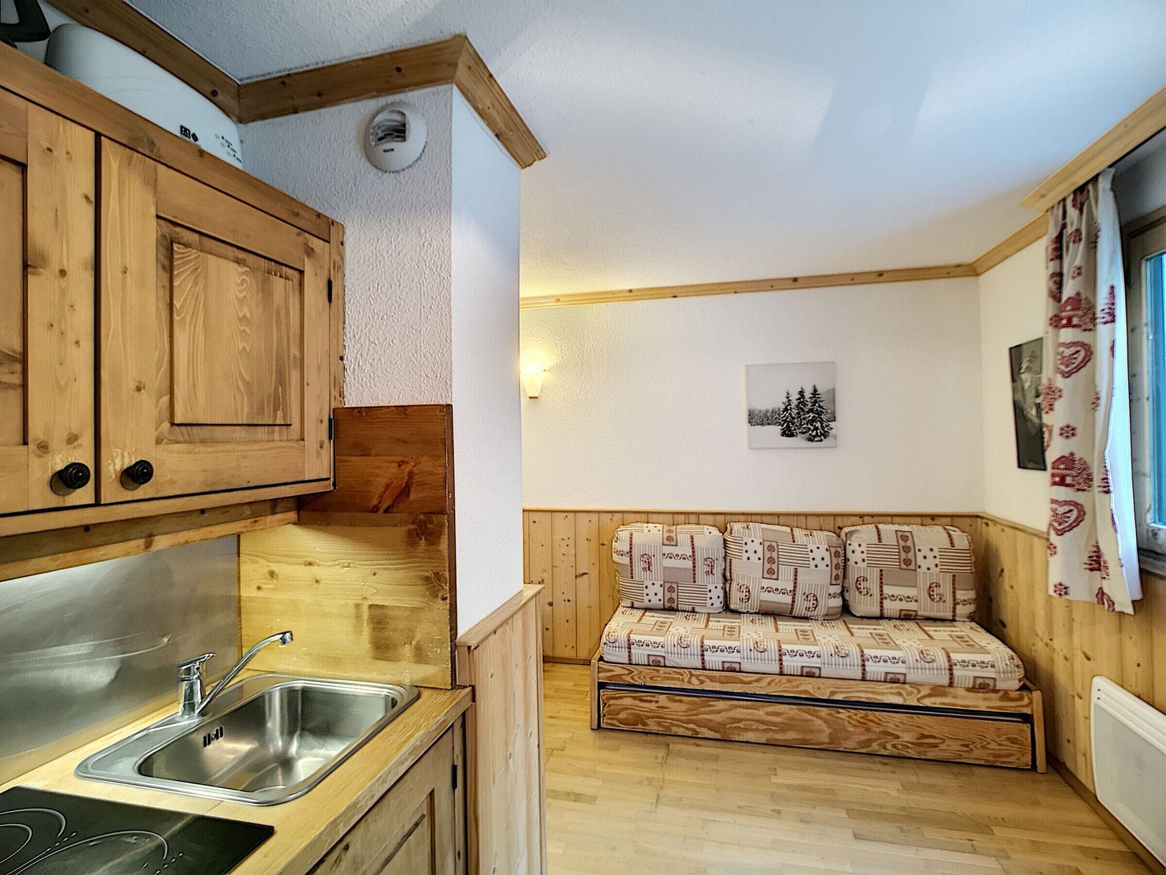 Une cuisine compacte avec des meubles en bois, un évier encastré et une petite fenêtre agrémentée de rideaux.