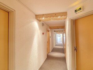 A hallway with a wooden ceiling, a sign indicating a secure exit, and doors on both sides. - Cozy Studio 2 Pers, Wifi, Pets Allowed, Parking (Les Menuires)