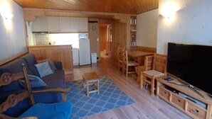 A wooden interior with a sofa, TV, dining table, and kitchen area. - Cozy 3-Room Apartment, South Exposure, Village Center, Sleeps 6 (La Clusaz)