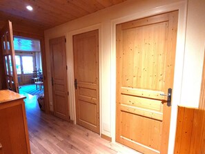 A hallway with wooden doors, a wooden desk, and a view into a room with a table and chairs.