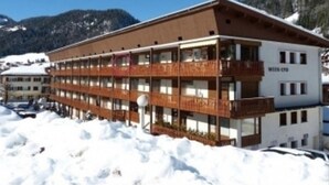 A multi-story building with a wooden facade, balconies, and a sign indicating "WELLS 190". - Cozy 3-Room Apartment, South Exposure, Village Center, Sleeps 6 (La Clusaz)