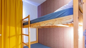 A bunk bed room with a wooden ladder, a yellow curtain, and a patterned wall.