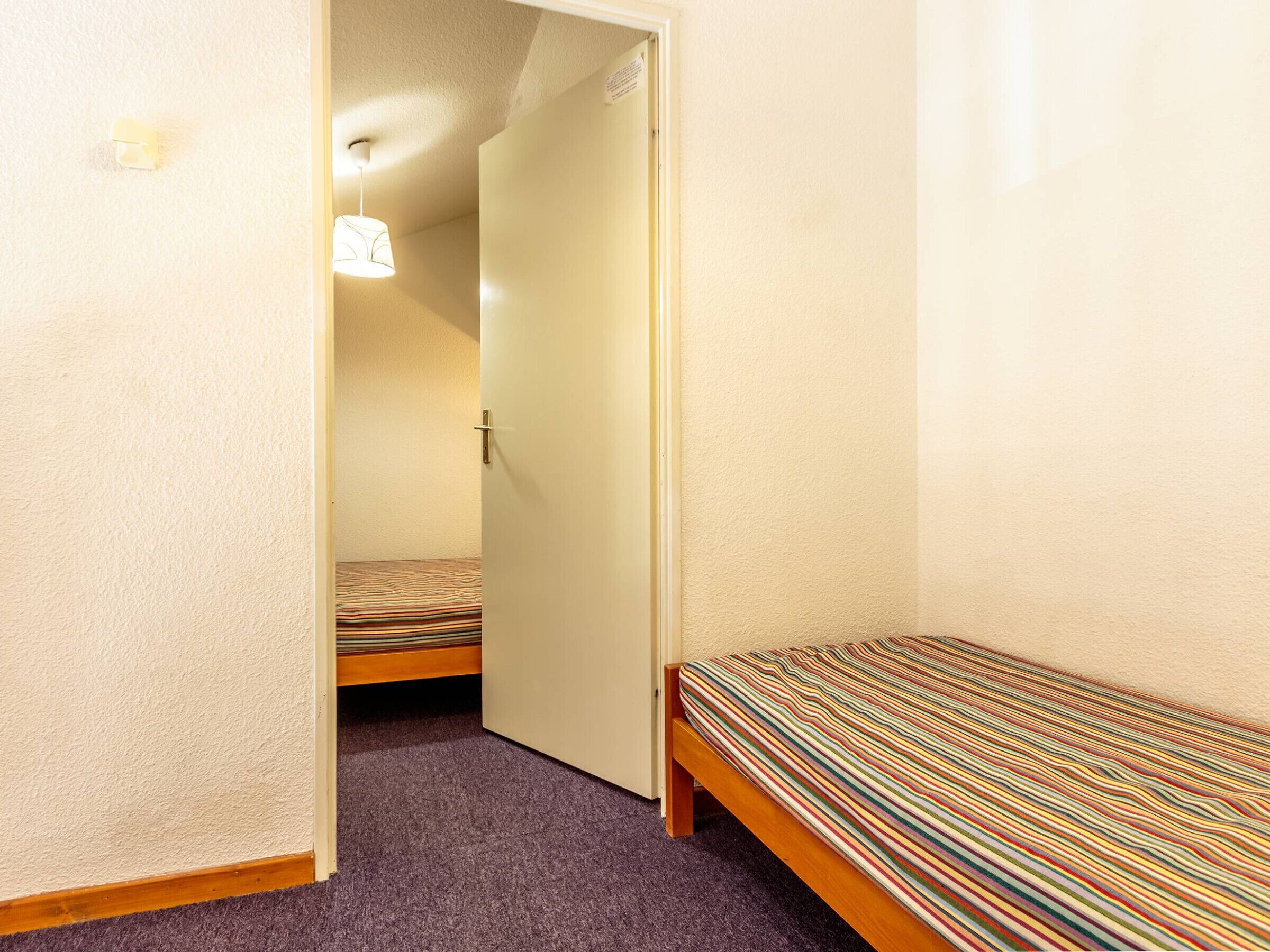 Een kleine, smalle kamer met een enkel bed en een deur naar een andere kamer.