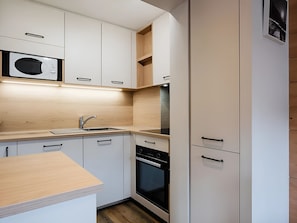 A compact kitchen with white cabinetry, a microwave, a sink, and a built-in oven.