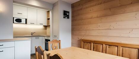 A modern kitchen with white cabinets, a wooden dining table, and a wooden wall.