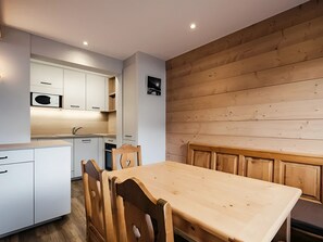 A modern kitchen with white cabinets, a wooden dining table, and a wooden wall.