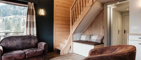 A modern interior with a wooden staircase, a sofa, and a view of a mountainous landscape.