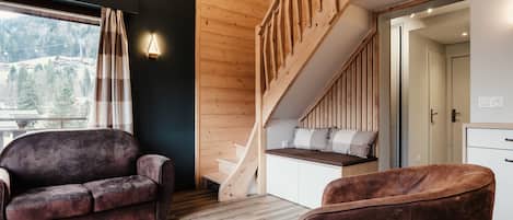 A modern interior with a wooden staircase, a sofa, and a view of a mountainous landscape.