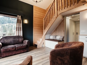 A modern interior with a wooden staircase, a sofa, and a view of a mountainous landscape.