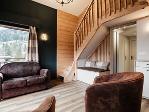 A modern interior with a wooden staircase, a sofa, and a view of a mountainous landscape.