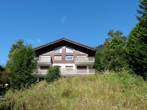 A multi-story building with balconies, surrounded by greenery.