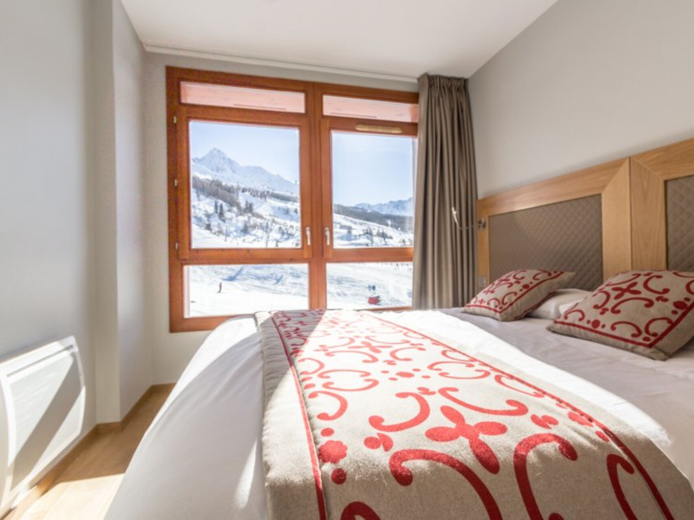 Una habitación de hotel con cama, un ventanal y vistas a la montaña, además de un cabecero de madera.