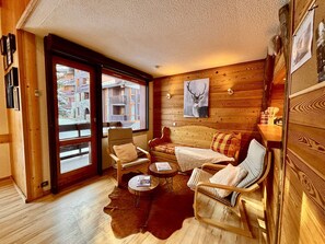 A cozy room with a wooden interior, a large window, a sofa, a chair, a small table, and a rug.
