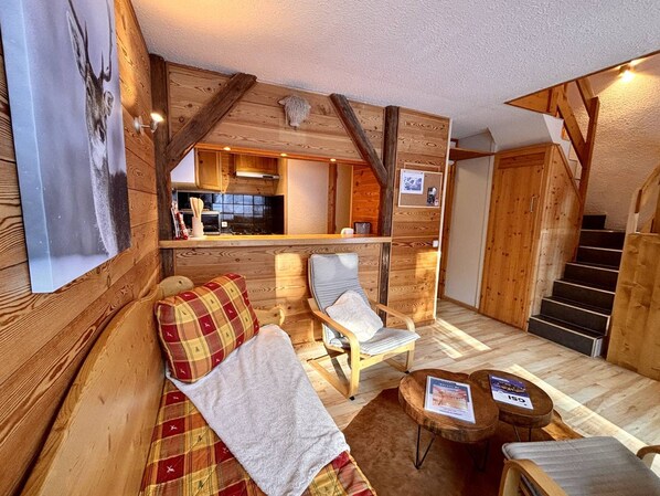A cozy cabin interior with a wooden interior, a sofa, a chair, a small table, and a staircase.