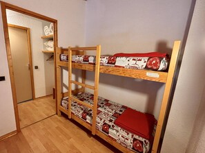 A bunk bed with patterned bedding, a wooden shelf unit, and a door.