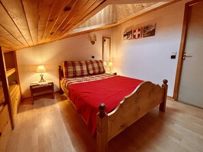 A bedroom with a wooden bed, two bedside tables with lamps, a red bedspread, and a Swiss flag on the wall. - Duplex 6 pers, central location, parking, pets OK (La Plagne)