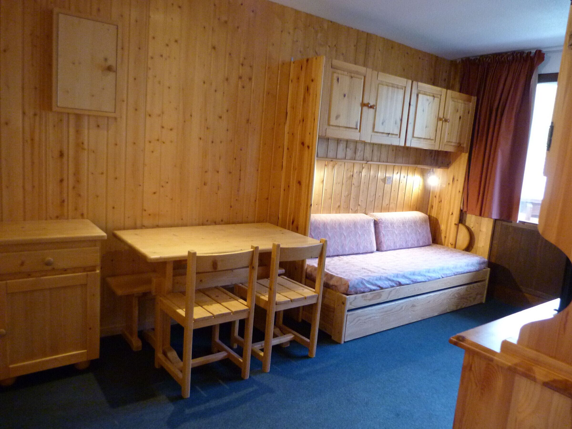 Une petite pièce comprenant un lit superposé en bois, une petite table et une chaise.