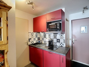 Compact kitchen with microwave, sink, and countertop with patterned backsplash.