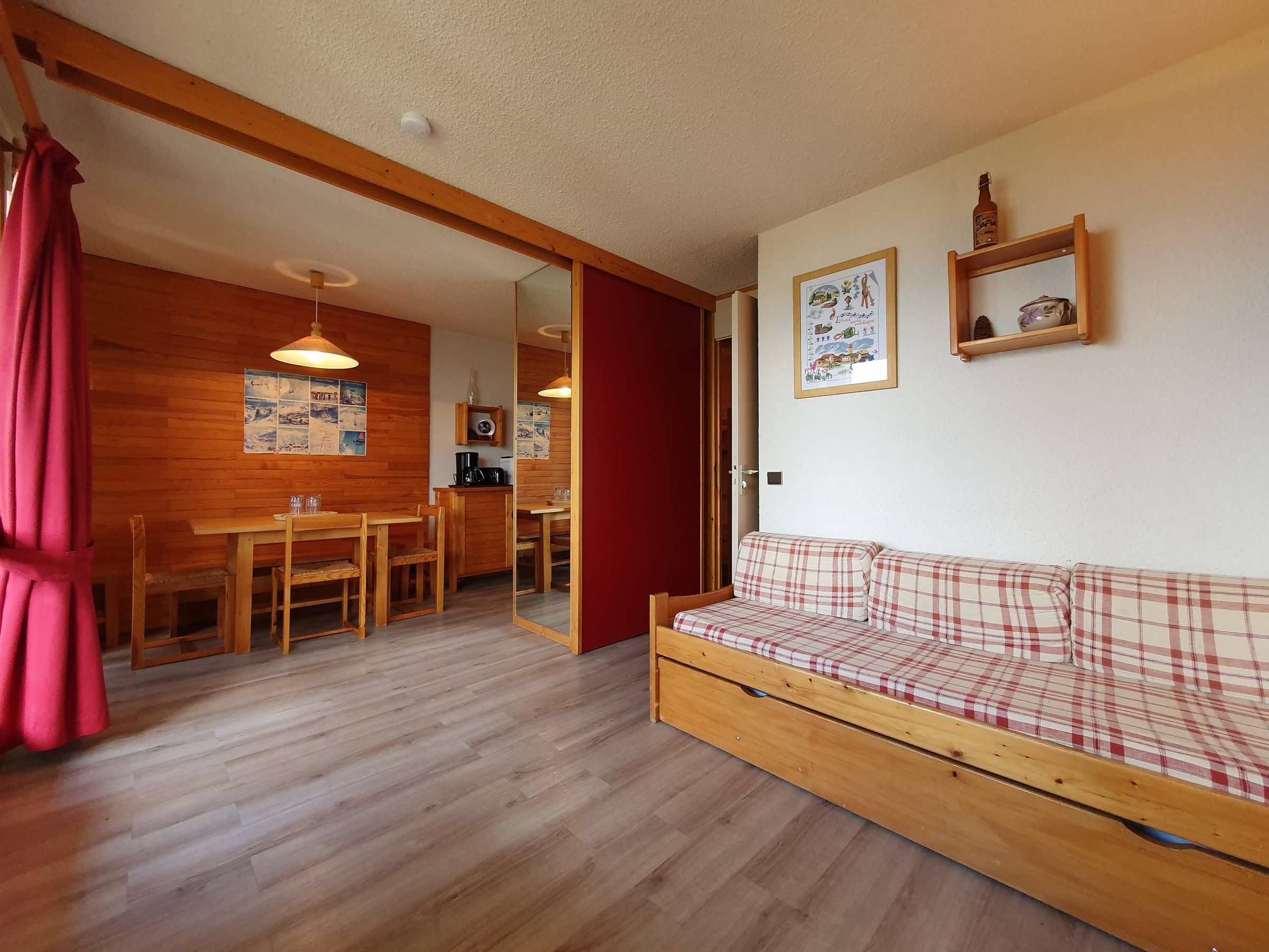 A cozy room with a wooden floor, a plaid sofa, a dining table with chairs, and a kitchen area.