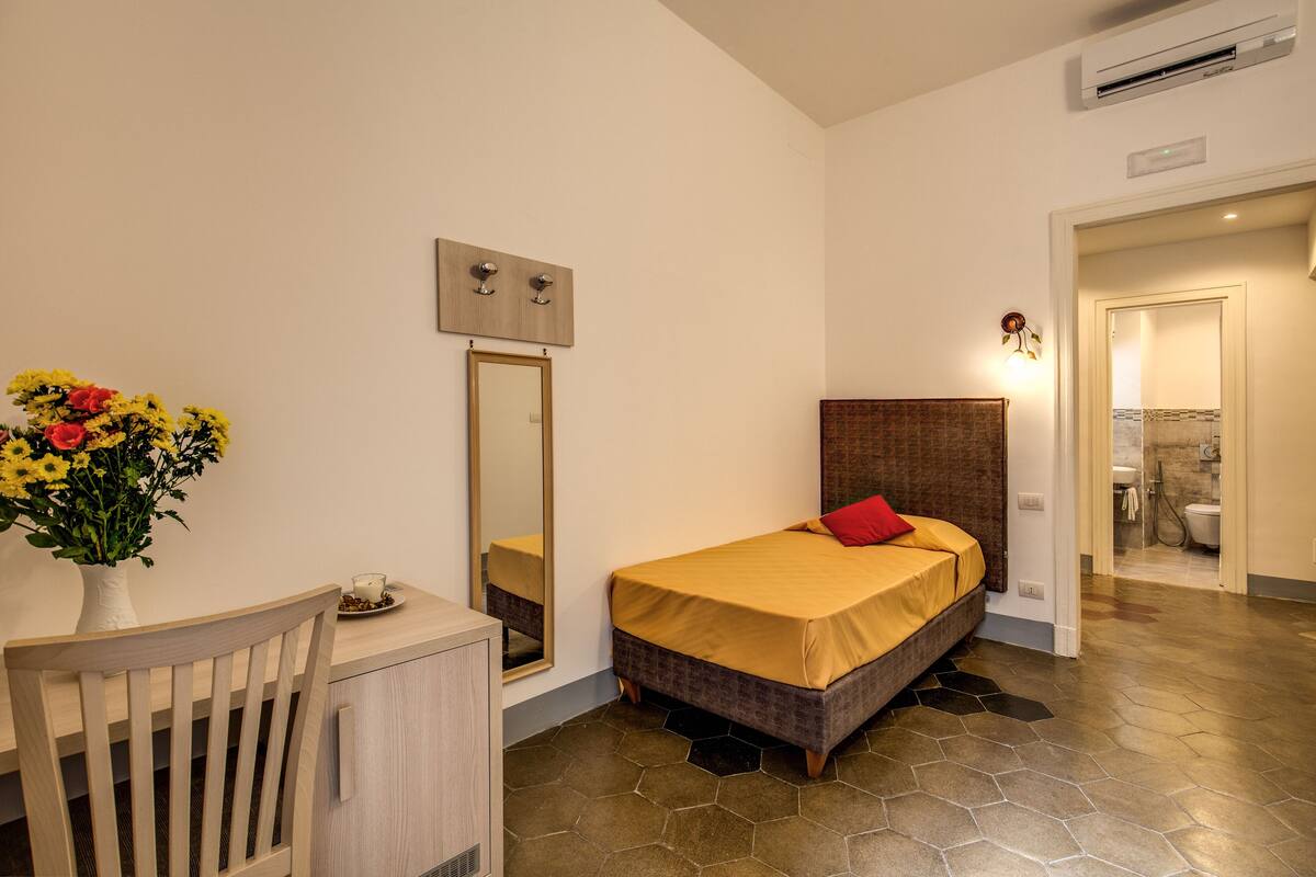 Ein Schlafzimmer mit Bett, Schreibtisch, Stuhl und einem Blumenstrauß.