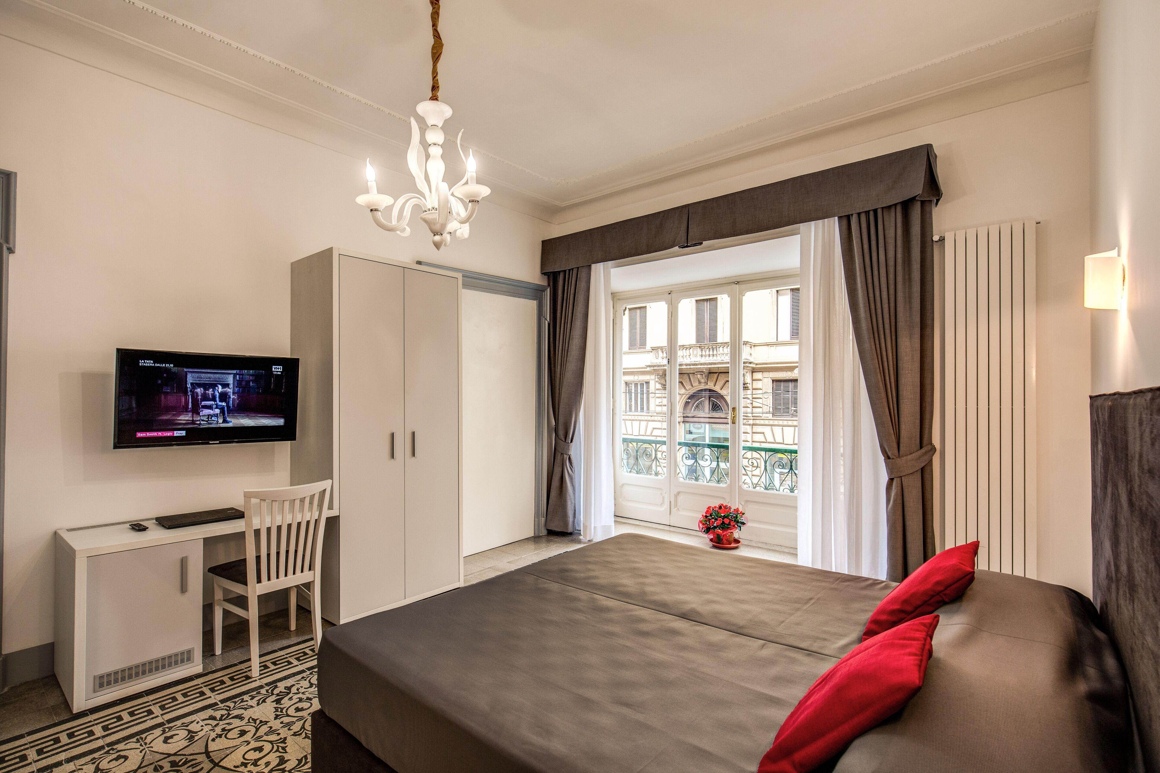 A hotel room with a bed, a desk, a television, and a view of the outside balcony.
