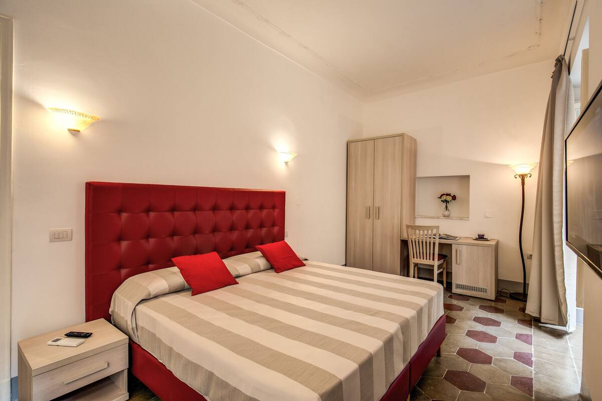 Ein Schlafzimmer mit rotem Kopfteil, einer gestreiften Bettdecke und einem Schreibtisch mit Stuhl.