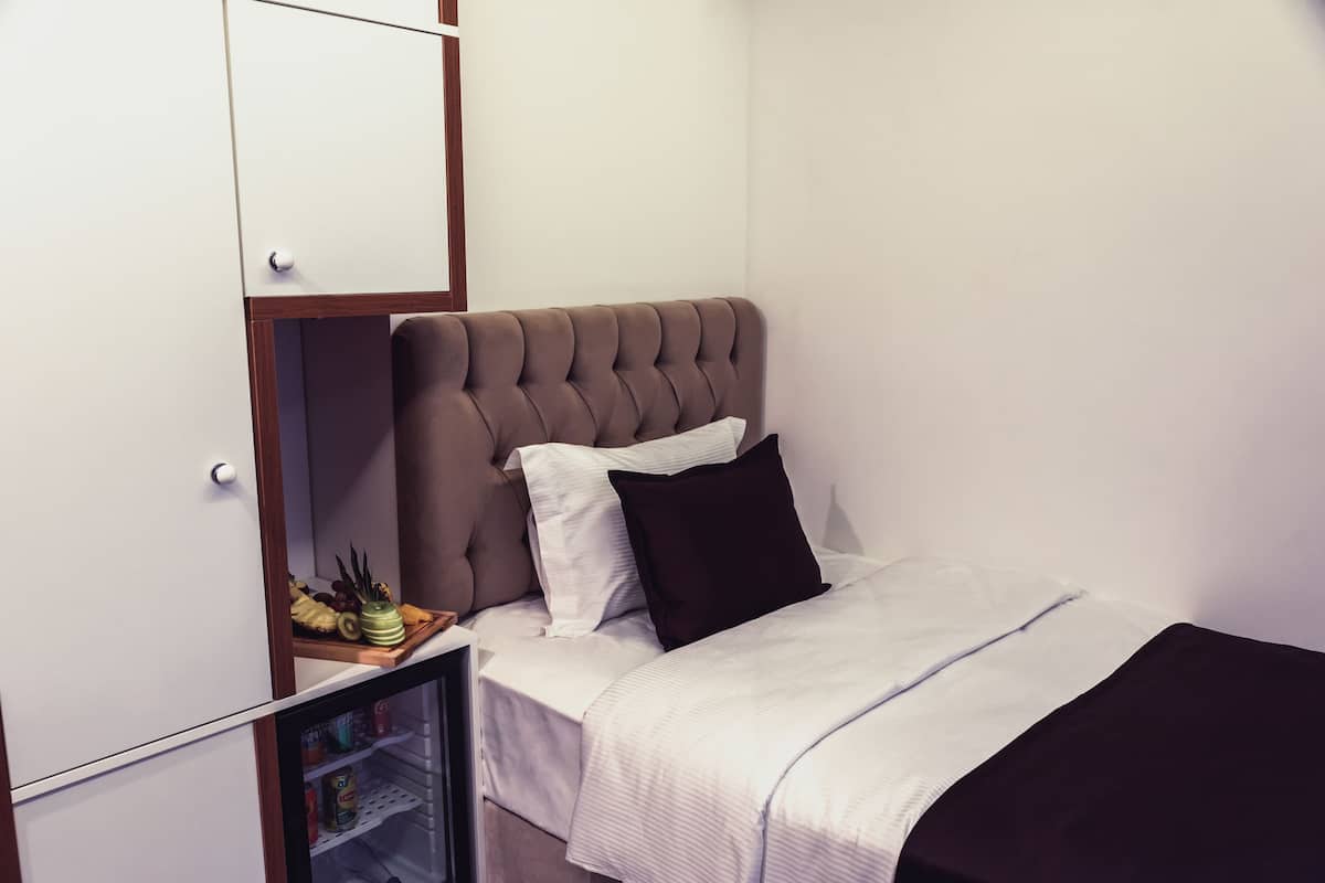 A bedroom with a bed, a wardrobe, and a small refrigerator.