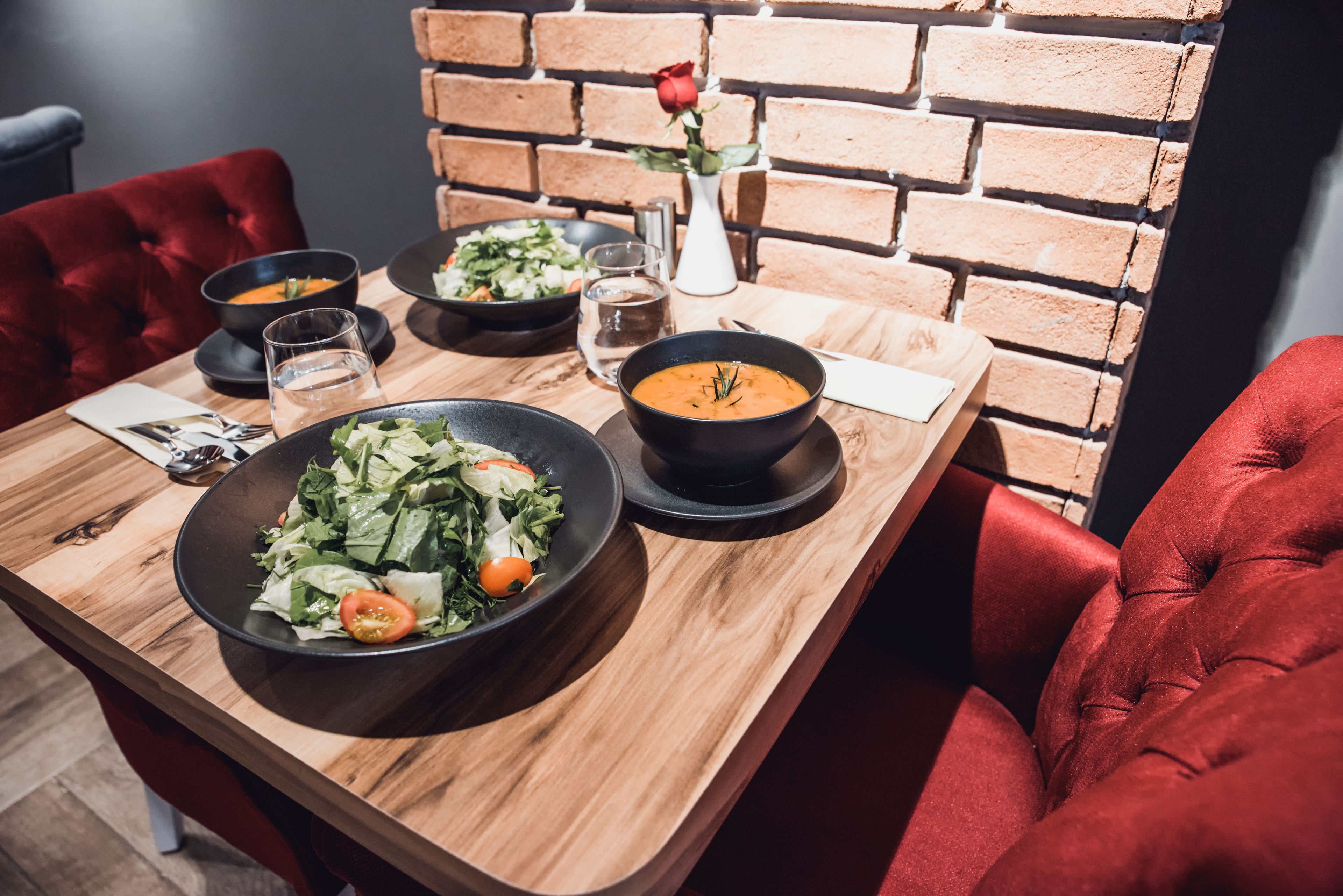 Ein Esstisch mit Salat, Suppe und einer Rose in einer Vase.