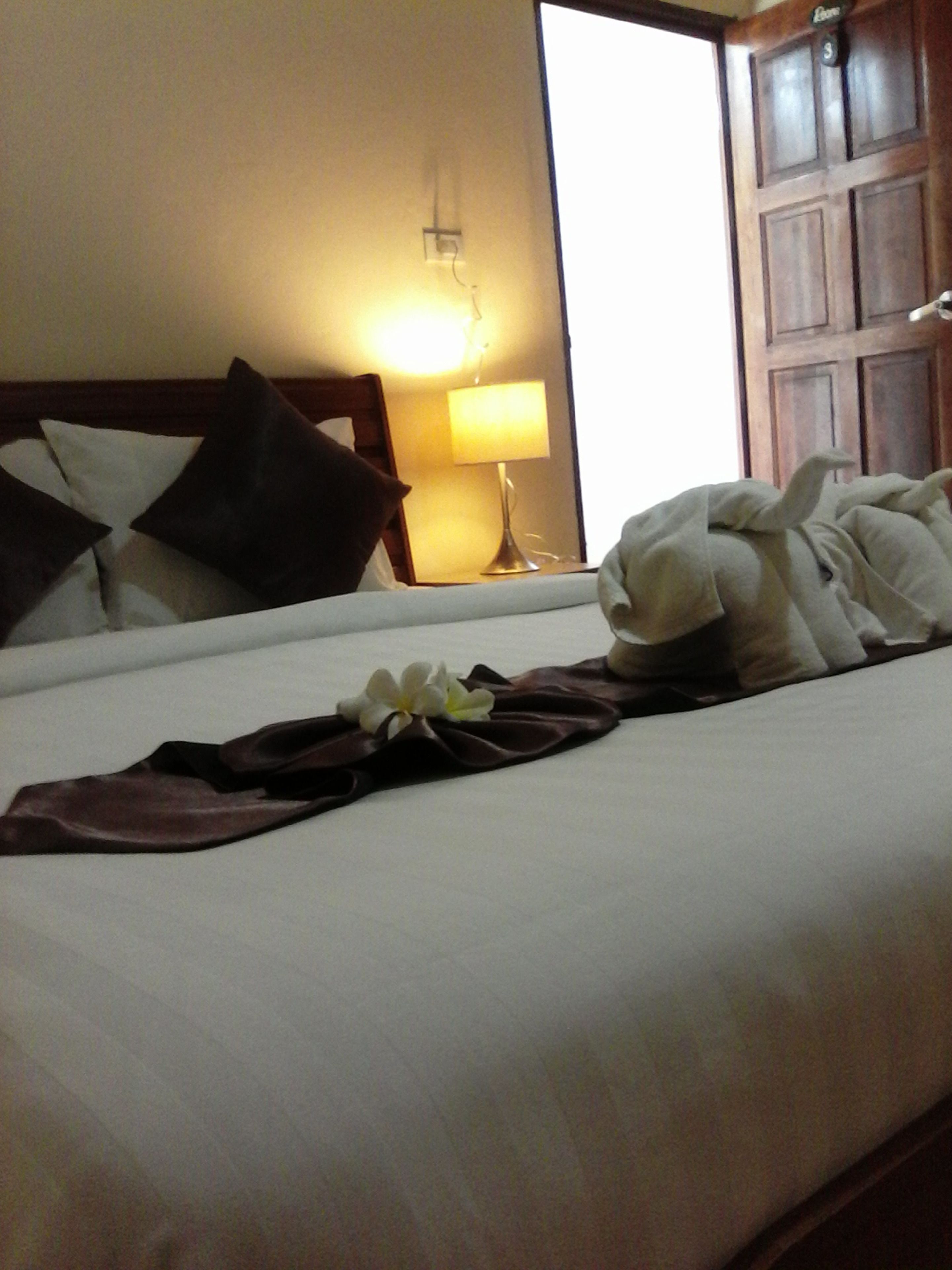 Una cama bien hecha con almohadas, una lámpara y una flor encima.