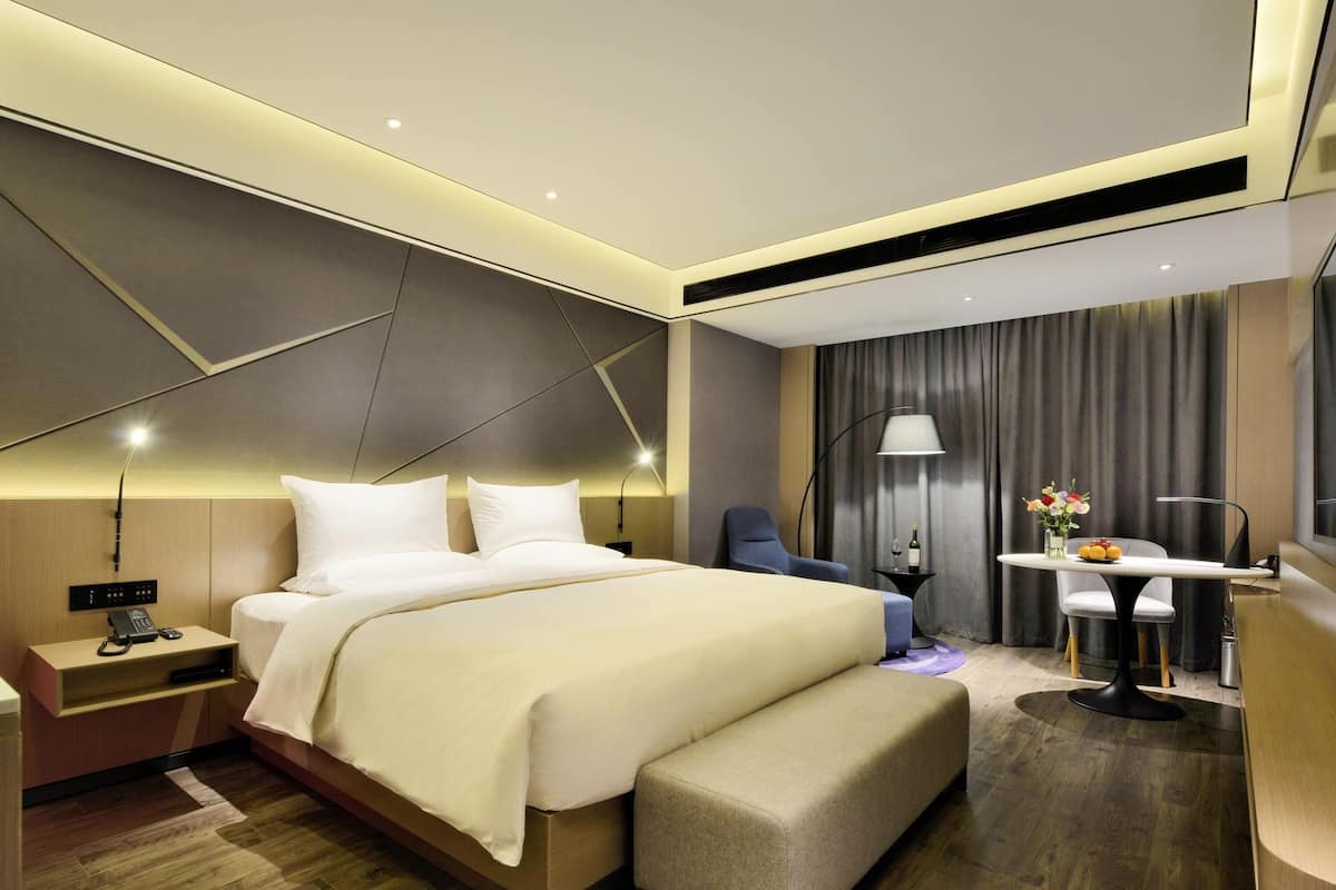 Een moderne hotelkamer met een groot bed, nachtkastje, lamp en een bureau met stoel.