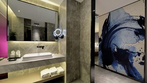 Un baño moderno con un espejo grande, un tocador con lavabo y un cuadro abstracto de gran tamaño en la pared.