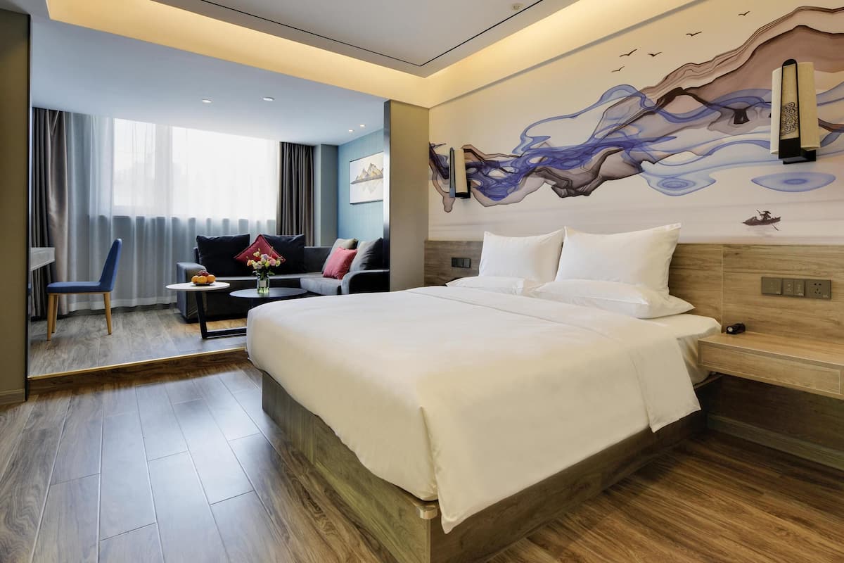 Een moderne hotelkamer met een groot bed, een slaapbank, een bureau en een wanddecoratie.