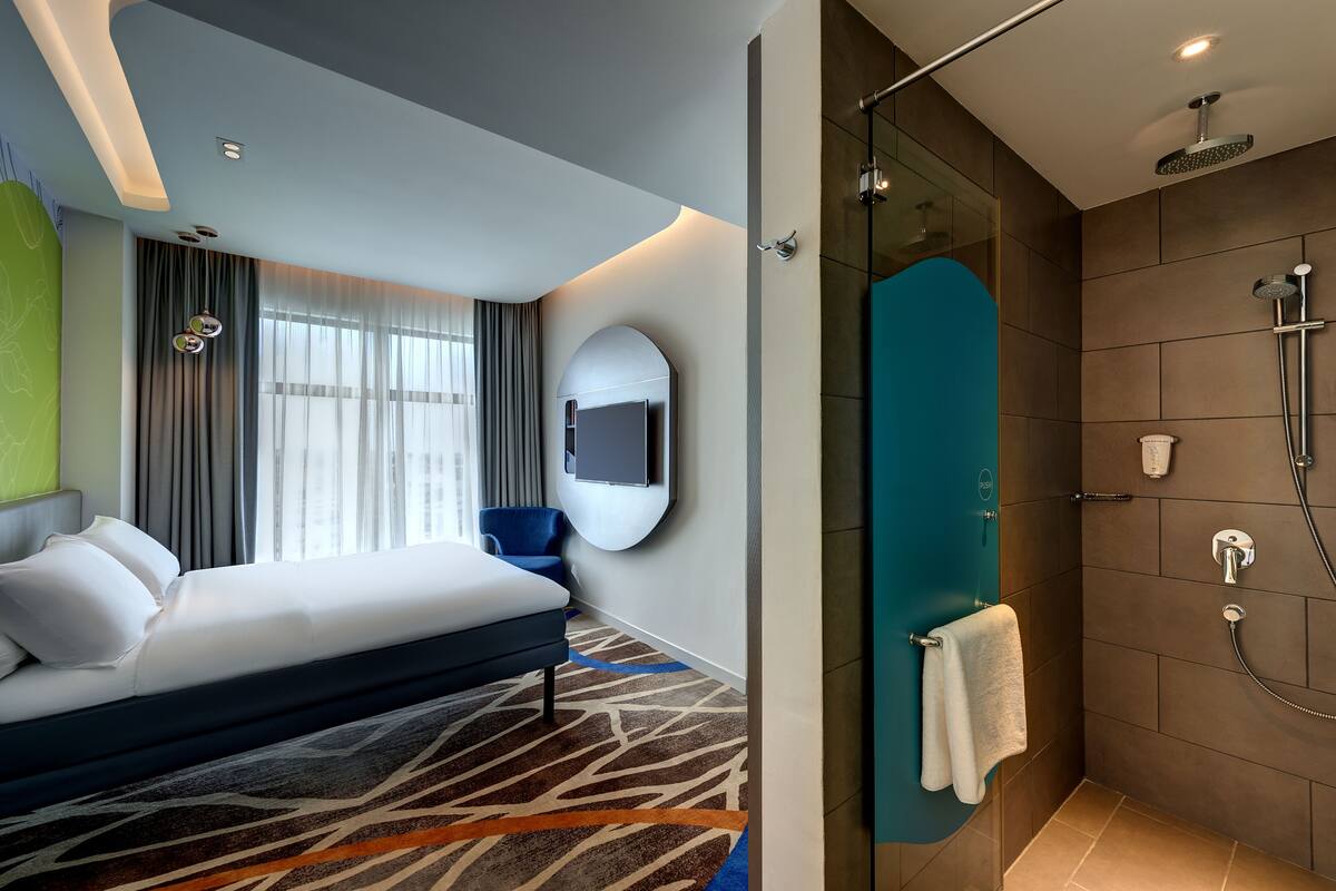 Een moderne hotelkamer met een groot bed, een douche en een aan de muur bevestigde televisie.