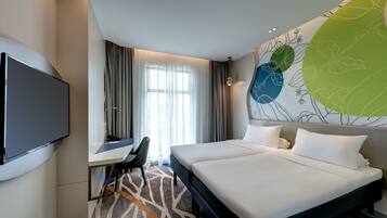 Een hotelkamer met een bed, een bureau, een televisie en een groot wanddecor.