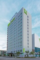 A modern hotel building with a prominent green 'ibis styles' sign, multiple floors, and a flat facade.