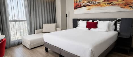Una habitación de hotel moderna con una cama grande, un sofá, una silla roja y un cuadro en la pared.