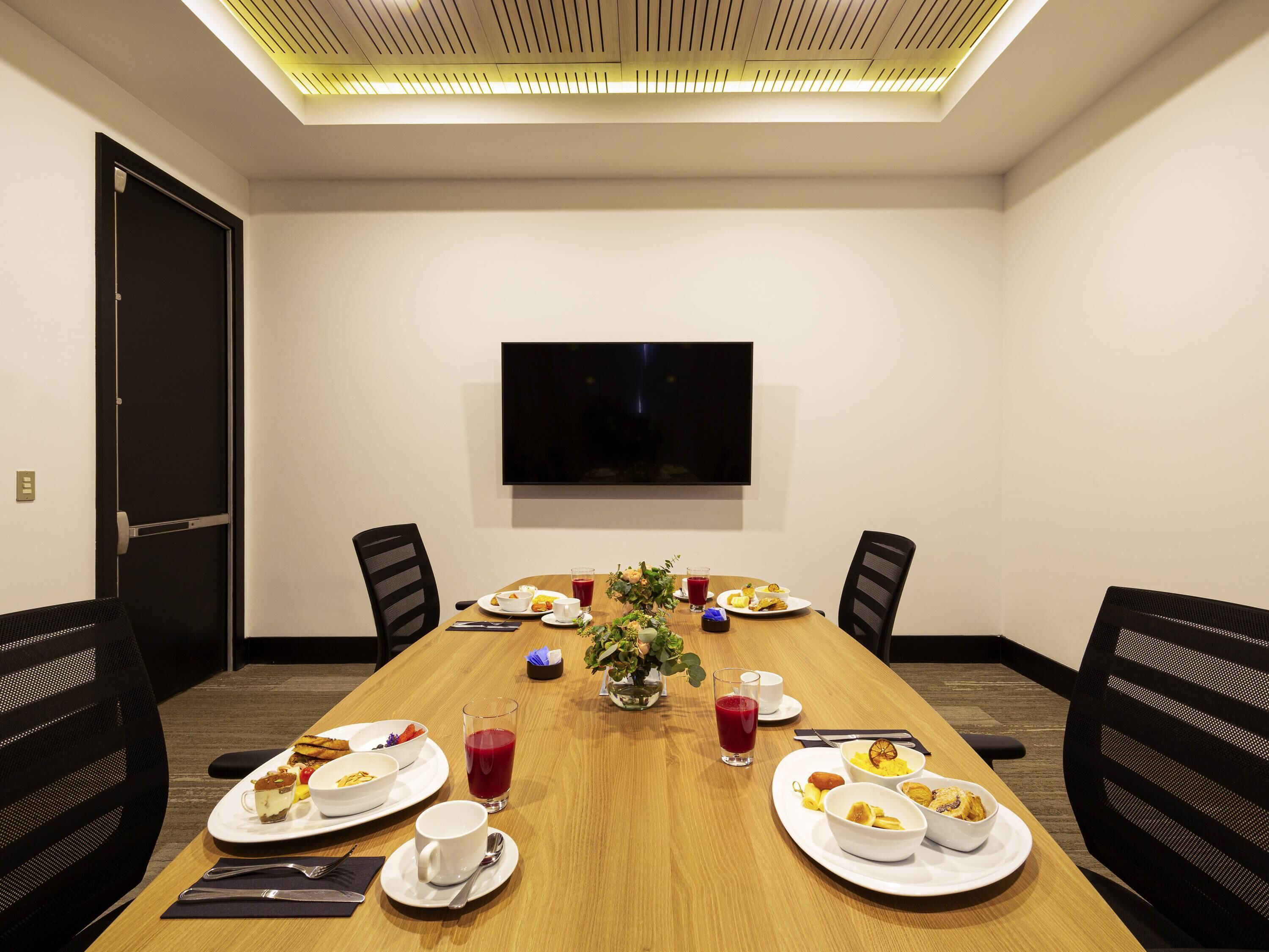 A conference room with a long table, chairs, a TV, and breakfast items.