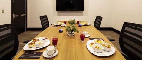 A conference room with a long table, chairs, a TV, and breakfast items.