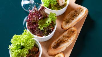 Una tabla de madera con cuatro ensaladas en cuencos y dos rebanadas de pan tostado, acompañada de una copa de vino.