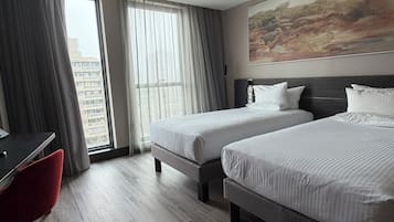 Una habitación de hotel con dos camas, un escritorio, una silla y un ventanal con cortinas.