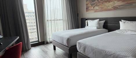 Een hotelkamer met twee bedden, een bureau, een stoel en een groot raam met gordijnen.